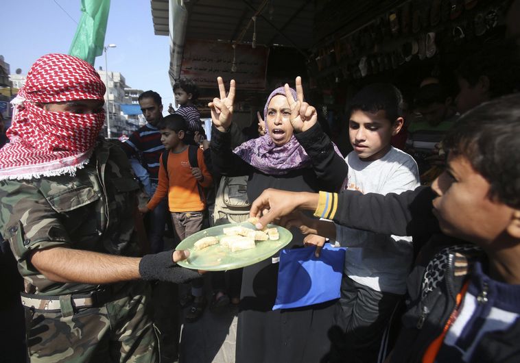 Masked Palestinian distributes sweets as he celebrates with others an attack on a Jerusalem synagogue, in Rafah in the southern Gaza Strip